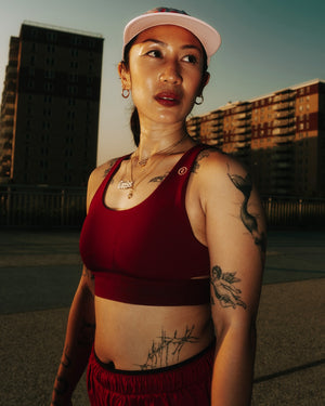 Person wearing a Ciele Athletics Women's QCKBra Sports Bra in Crimson Red Maroon sports bra standing in an urban setting.