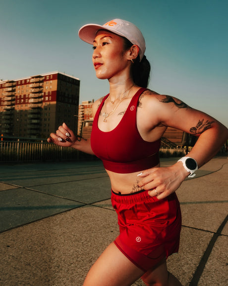 Woman in a Ciele Athletics Women's QCKBra Sports Bra in Crimson Red Maroon sports bra running outdoors with buildings in the background