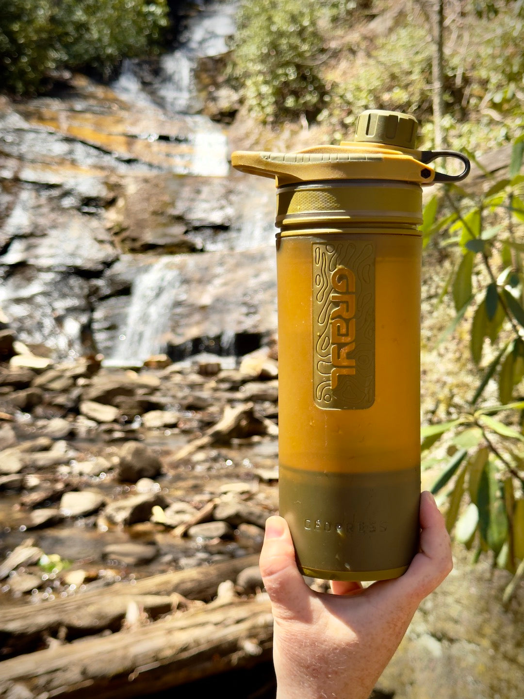 Grayl Geopress Water Purifier Bottle being held in front of a waterfall.