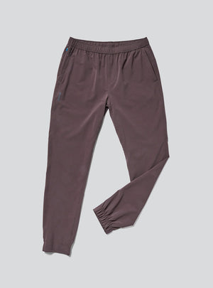 Janji Men's Transit Tech Pant in Loam on a neutral background.