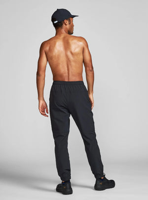 Janji Men's Transit Tech Pant in Midnight worn by a man from the rear on a neutral background.