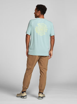 Janji's Circa Daily Tee in Destination Everywhere worn by a man on a neutral background, showing the image on the back of the shirt.