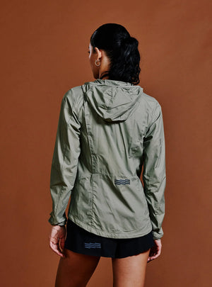 Janji W's Zephyrunner Wind Shell in Sage being worn by a woman from the rear on a neutral background.