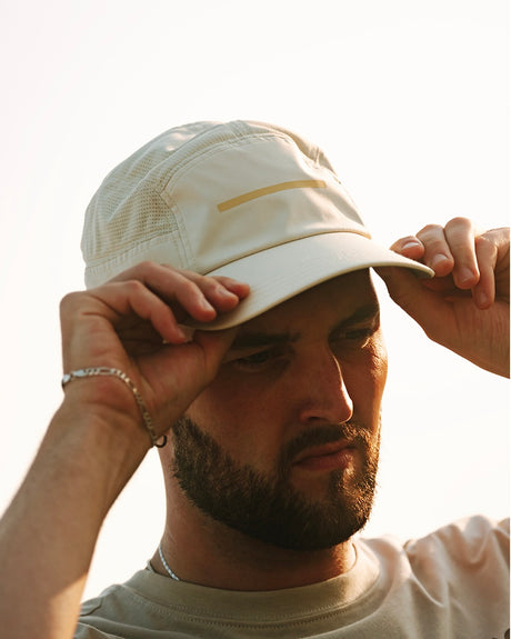 Man adjusting a ciele athletics GOCap Comp - Bars Glade light yellow running cap against a neutral background