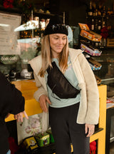 Janji Multipass Sling Bag being worn by a woman in a store as a crossbody bag.