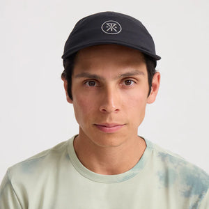 Man wearing a Roark Alta Elite Run Hat Strapback Hat in Black with a logo on a white background