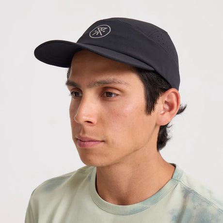 Man wearing a Roark Alta Elite Run Hat Strapback Hat in Black with a logo on a white background