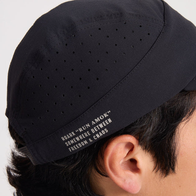 Roark Alta Elite Run Hat Strapback Hat in Black with text on the strap worn by a person, against a neutral background