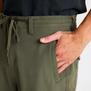 Person wearing Roark Layover Pro Traveler Pants in Military with a hand in the pocket against a white background