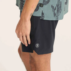 Person wearing Roark Serrano 7" Active Stretch Shorts in Black with a brand logo on a plain background
