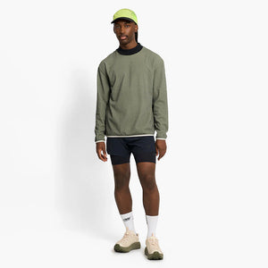 Man wearing a ciele athletics VLVMockneck Fleece Running Sweatshirt in Glade, black shorts, and a green cap on a white background