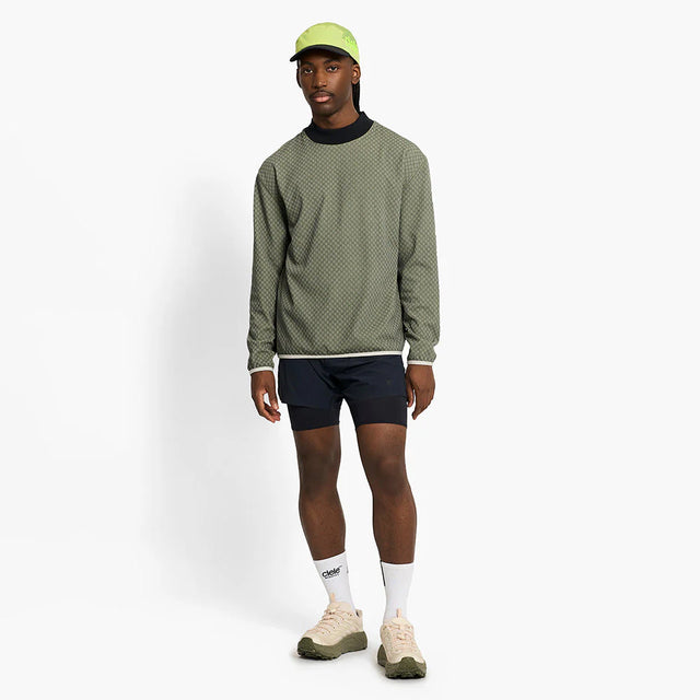 Man wearing a ciele athletics VLVMockneck Fleece Running Sweatshirt in Glade, black shorts, and a green cap on a white background