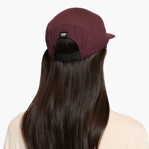 Person wearing a maroon ciele athletics GOCap Classic - Athletics in Dark Wine Red with a brand logo on a white background