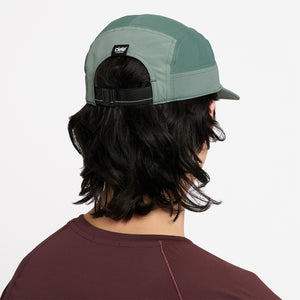 Person wearing a Ciele Athletics GOCap Comp Century Silver Pine green running cap on a white background