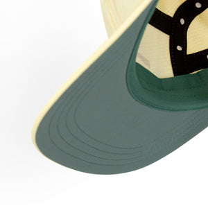 Close-up of a ciele athletics GOCap Comp - Bars Glade light yellow running cap with a green brim and beige top on a white background