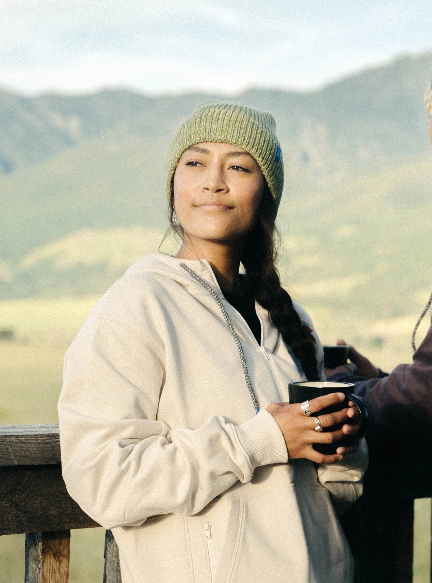 Janji Threshold Melange Beanie in Golden Ridge worn by a woman outdoors.