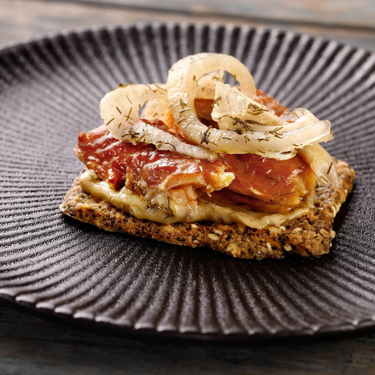Close-up of a sandwich with Fangst Faroe Islands Salmon Smoked Over Beech Wood on a textured black plate.