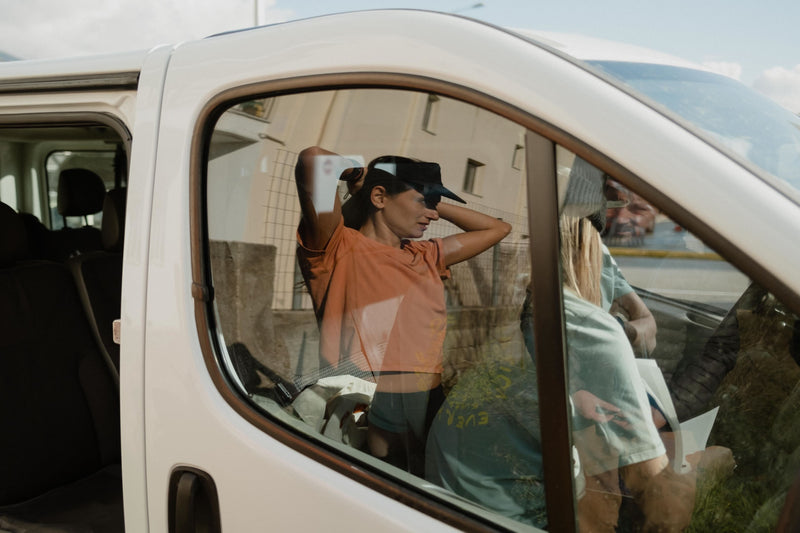 Janji's Circa Boxy Daily Tee in Amphora being worn by a woman in the reflection of a car window.