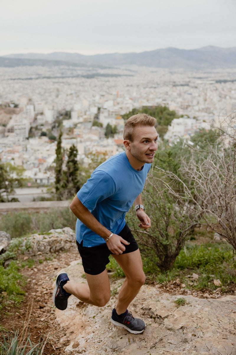 Janji's Circa Daily Tee in Aegean being worn by a man running outdoors on a trail.