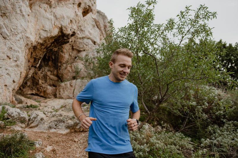 Janji's Circa Daily Tee in Aegean being worn by a man running on a trail.