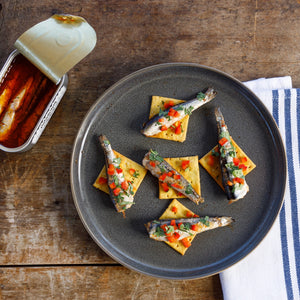 Plated appetizers with a can of Patagonia Provisions Spicy White Anchovies on a wooden surface
