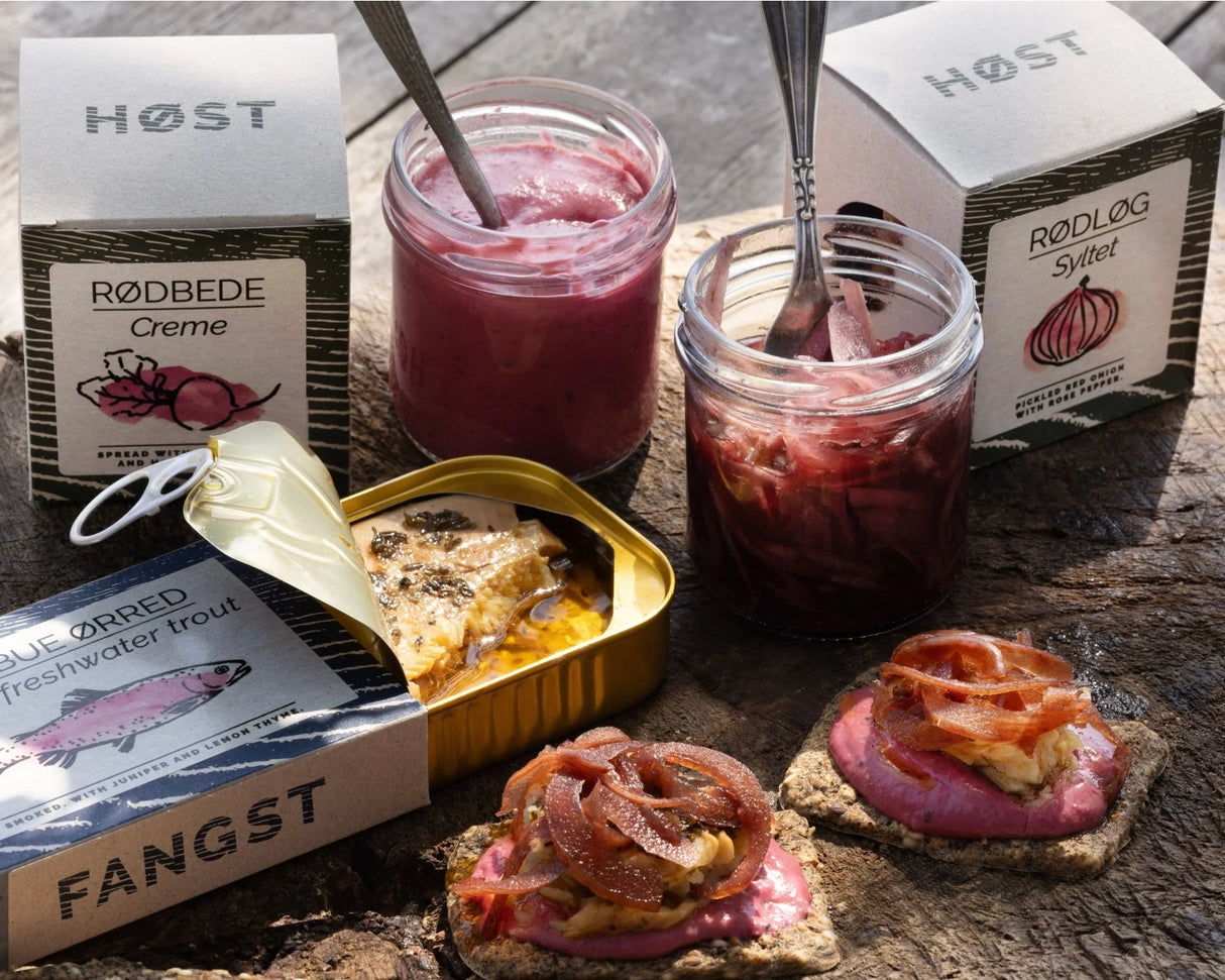 Jars of pickled vegetables with Fangst Danish Smoked Trout with Juniper & Lemon Thyme on a wooden surface.