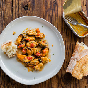 Patagonia Provisions Spicy Mussels tinned fish on a plate with bread on a wood background.