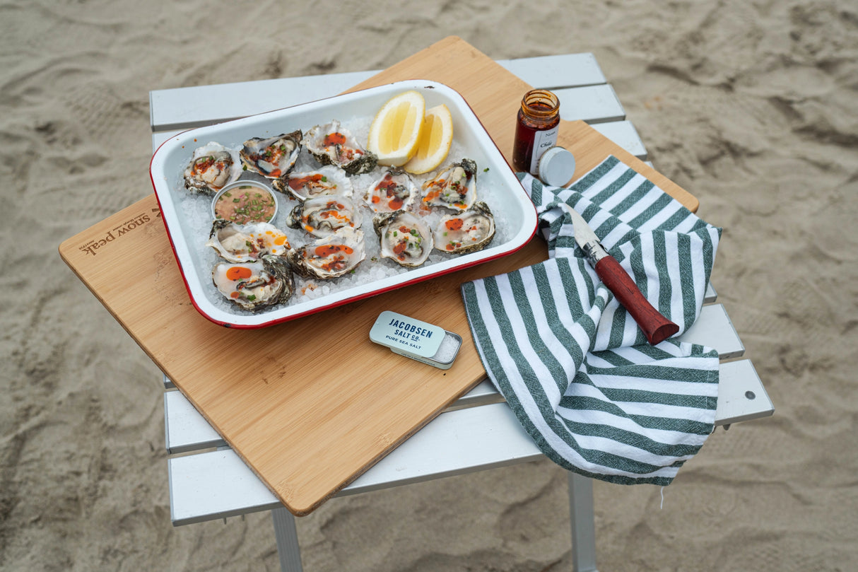 Tray of oysters on a beach setting with Jacobsen Salt Co. Kosher Sea Salt Slide Tin.
