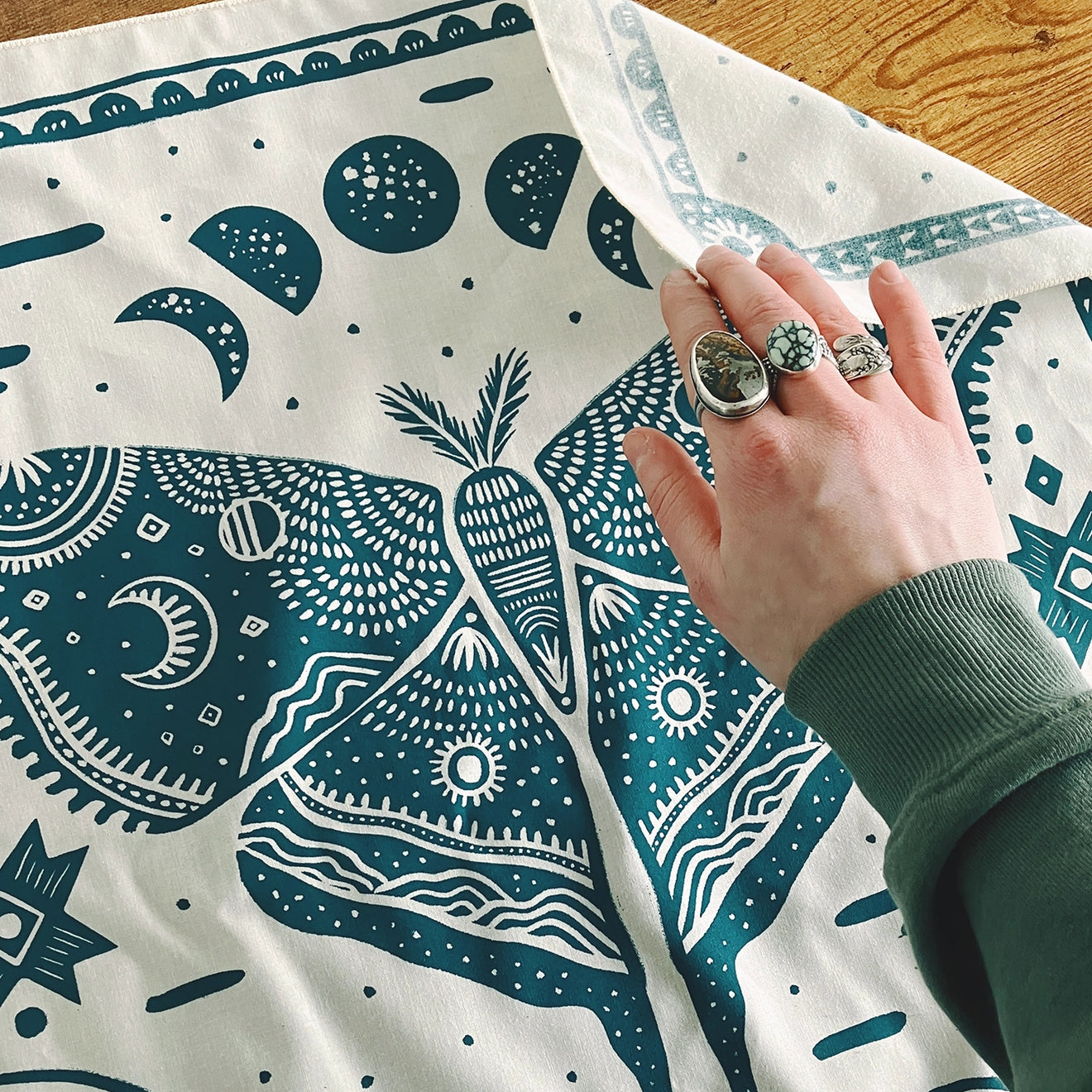 Land & She Luna Moth Bandana on a wood background with a hand.