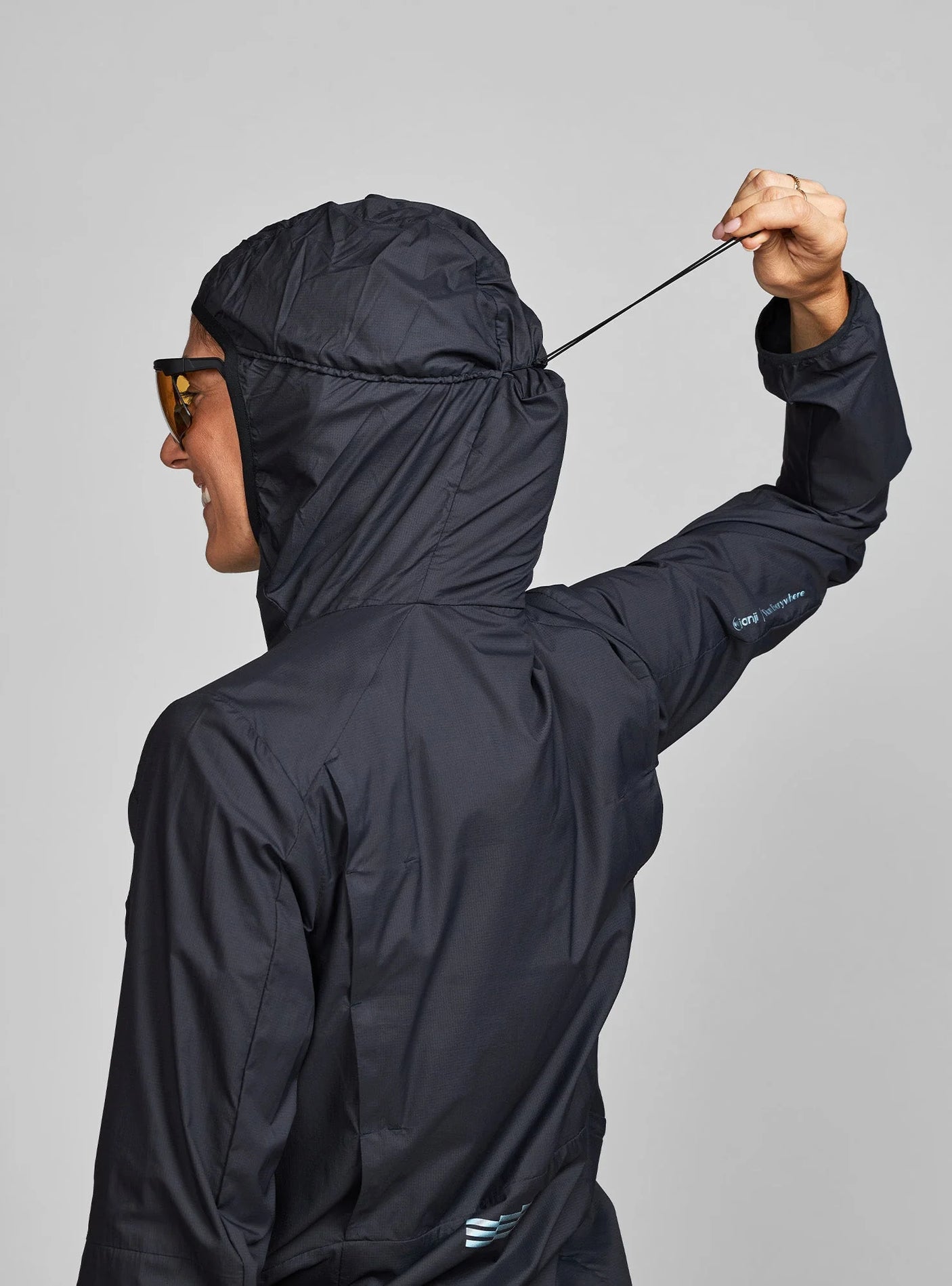 Janji W's Zephyrunner Wind Shell in Midnight showing the hood cinch on a neutral background.