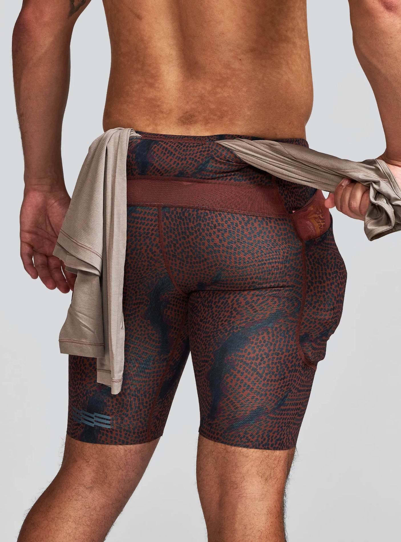 Janji Men's 8" Trail Half Tight in Shadowlands showing the rear pass-thru pocket on a neutral background.