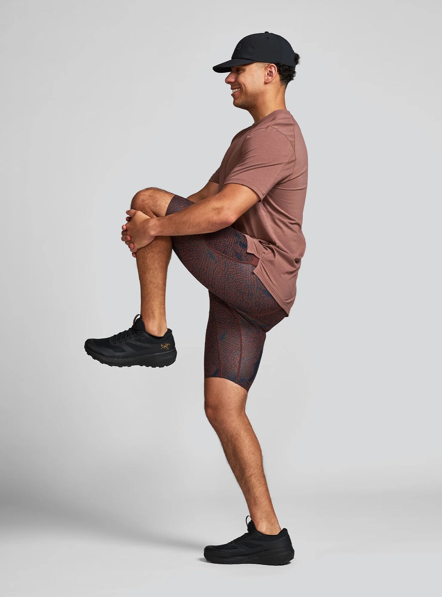 Janji Men's 8" Trail Half Tight in Shadowlands worn by a man stretching on a neutral background.