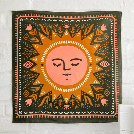 Land & She Sun Still Rises Bandana on a neutral brick background.