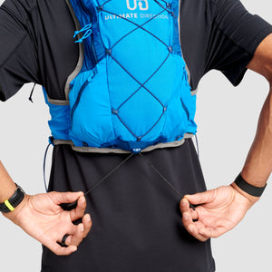 The Ultimate Direction Ultra Vest 6.0 on a neutral background being worn by a man and showing the bungee system.